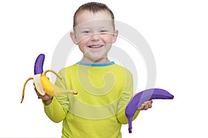 Happy smiling child holding purple bananas in his hands. The concept is childish spontaneity, it is unique and unusual, like these