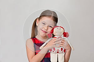 Happy and smiling child hugging doll toy on grey background caucasian little girl kid of 6 7 years in red plaid dress