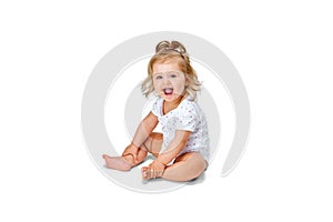 Happy, smiling child. Little baby girl, toddler sitting on floor and cheerfully laughing against white studio background