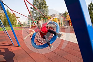 Happy smiling child swinging on a swing with closed eyes and arms outstretched at playground