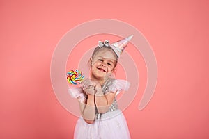 Happy smiling child with tasty lollipop having fun over pink background.