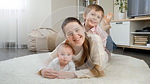 Happy smiling children hugging and having fun with mother on carpet in living room. Parenting, children happiness and