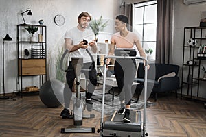 Happy smiling couple doing cardio on stationary bike and treadmill using smart phone