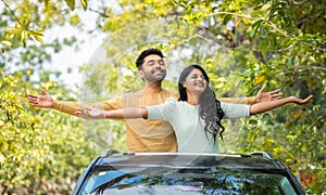 Happy smiling couple feeling nature fresh air by stretching arms on car sunroof - concept of togetherness, weekend