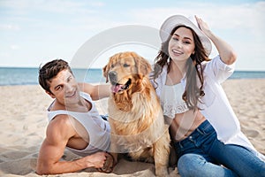 Happy smiling couple in love sitting on beach with dog
