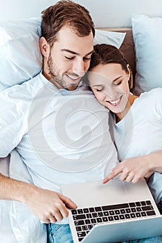 Smiling couple lying on bed and using laptop