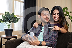 Happy smiling couple making online purchase by talking eachother on mobile phone by using credit card at home - concept