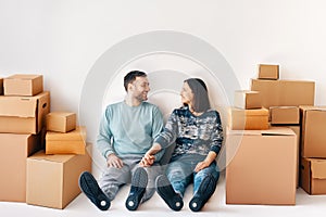 Happy smiling couple at new home sitting on floor surrounded by cardboard boxes