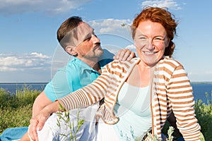 Happy Smiling Couple Relaxing on Green Grass and blue sky. Young Couple Lying on Grass Outdoor with water and sky background.