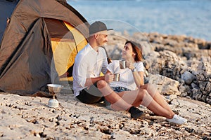 Happy smiling couple sitting face to face at rocky beach on near tent.