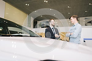 Happy smiling customer and friendly salesman are discussing new car in auto dealership.