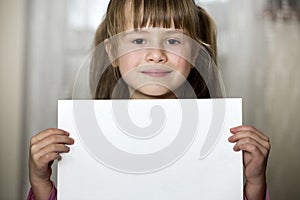 Happy smiling cute child girl holding white copy space sheet of drawing paper. Art education, creativity, advertisement concept