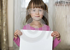 Happy smiling cute child girl holding white copy space sheet of drawing paper. Art education, creativity, advertisement concept