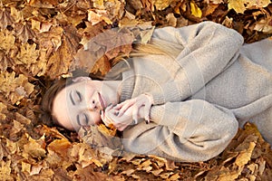 Happy smiling cute girl with closed eyes liying in the autumn leaves and enjoying it, holding face and smiling. Autumn portrait in