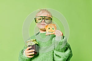 Happy smiling cute kid, little girl in fashionable look clothes and sunglasses with toast and jam over light green