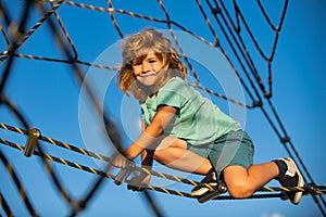 Happy smiling cute little child boy play monkey bars on the web in outdoor playground. Kids in rope park. Funny kids