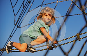 Happy smiling cute little child boy play monkey bars on the web in outdoor playground. Kids in rope park. Funny kids