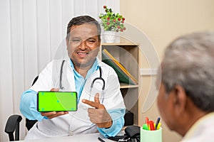 happy smiling doctor at hospital shownig green screen mobile phone to patient - concept of app promotion, advertisement