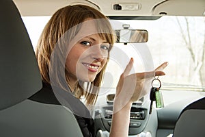 Happy smiling driver woman showing car key sitting in a new auto