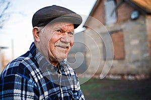 Happy smiling elder senior man portrait with a mustache in a cap on the background of a brick house in a Russian village