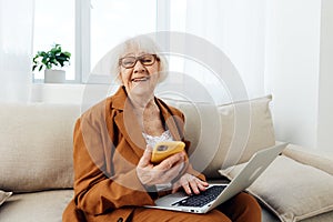 a happy, smiling elderly, gray-haired woman with a pleasant wide smile is sitting on a beige sofa in a brown suit