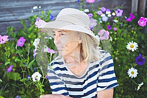 Happy smiling elderly senior woman having fun posing in summer garden with flowers in straw hat. Farming, gardening, agriculture,