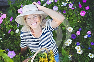 Happy smiling elderly senior woman having fun posing in summer garden with flowers in straw hat. Farming, gardening, agriculture,