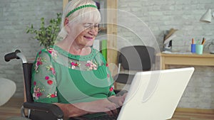 Happy smiling elderly woman disabled in a wheelchair uses a laptop close up