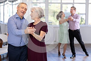 Happy smiling elderly woman enjoying impassioned merengue with male partner in latin dance salon. Social dancing concept