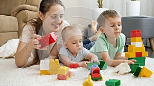 Happy smiling family with baby playing on carpet with toy blocks, bricks and cars. Concept of family having time