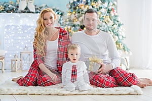 Happy smiling family in checkered pajamas near the Christmas tree and New Year`s fireplace