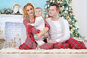 Happy smiling family in checkered pajamas near the Christmas tree and New Year`s fireplace