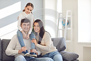 Happy smiling family. Daughter sits on fathers shoulders with mother sitting on the sofa