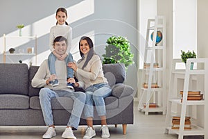 Happy smiling family. Daughter sits on fathers shoulders with mother sitting on the sofa