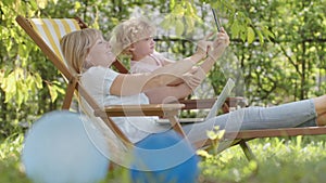 Happy smiling family in green garden, sunny summer day. Mom uses cell phone take a selfie with her little girl child. Together