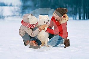 Happy smiling family having fun together in winter day, mother and child walking with white Samoyed dog