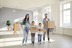 Happy smiling family with kids carrying cardboard boxes while moving into new home