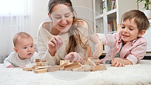 Happy smiling family playing with toy wooden blocks on carpet at home. Parenting, children happiness and family