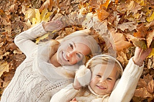 Happy smiling family portrait, mother and daughter have a rest laying on maple leaves in forest