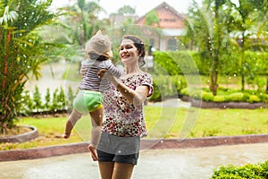 Happy smiling family under summer rain. Mother and little child girl have fun time while playing outdoors under warm