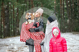 Happy, smiling family of woman, two children, cavalier king Charles dog, wrapped in warm clothes get warm in cold forest