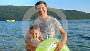 Happy smiling father with his son standing on beach with inflatable swimming ring. Family holidays, vacations