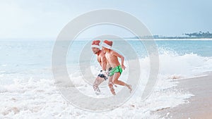 Happy smiling father and son wearing in Santa hats run together