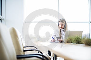 Happy smiling female customer support phone operator at workplace make notice in notebook.