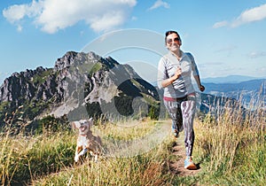 Happy smiling female jogging by the mounting range path with her beagle dog. Canicross running healthy lifestyle concept image