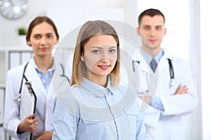 Happy smiling female patient with two cheerful doctors in the background. Medical and health care concept