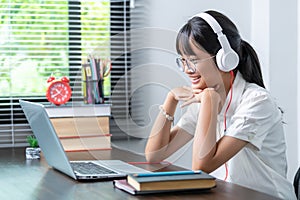 Happy smiling female student wearing headphones talking in online discussion meeting using laptop in home office. female college