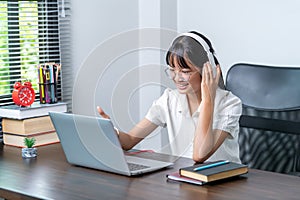 Happy smiling female student wearing headphones talking in online discussion meeting using laptop in home office. female college