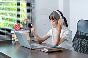 Happy smiling female student wearing headphones talking in online discussion meeting using laptop in home office. female college