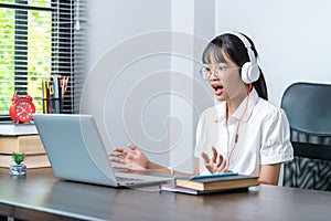 Happy smiling female student wearing headphones talking in online discussion meeting using laptop in home office. female college